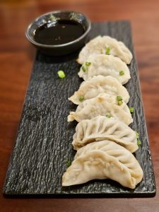 A row of freshly steamed chicken dumplings (momos) is served on a black stone platter with a bowl of dipping sauce. The simple presentation and soft texture make this dish look warm and inviting. Captured in Mankavu, Kozhikode.