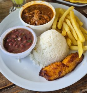 A white plate with white rice, French fries, a bowl of meat in red sauce, and a bowl of red bean stew.