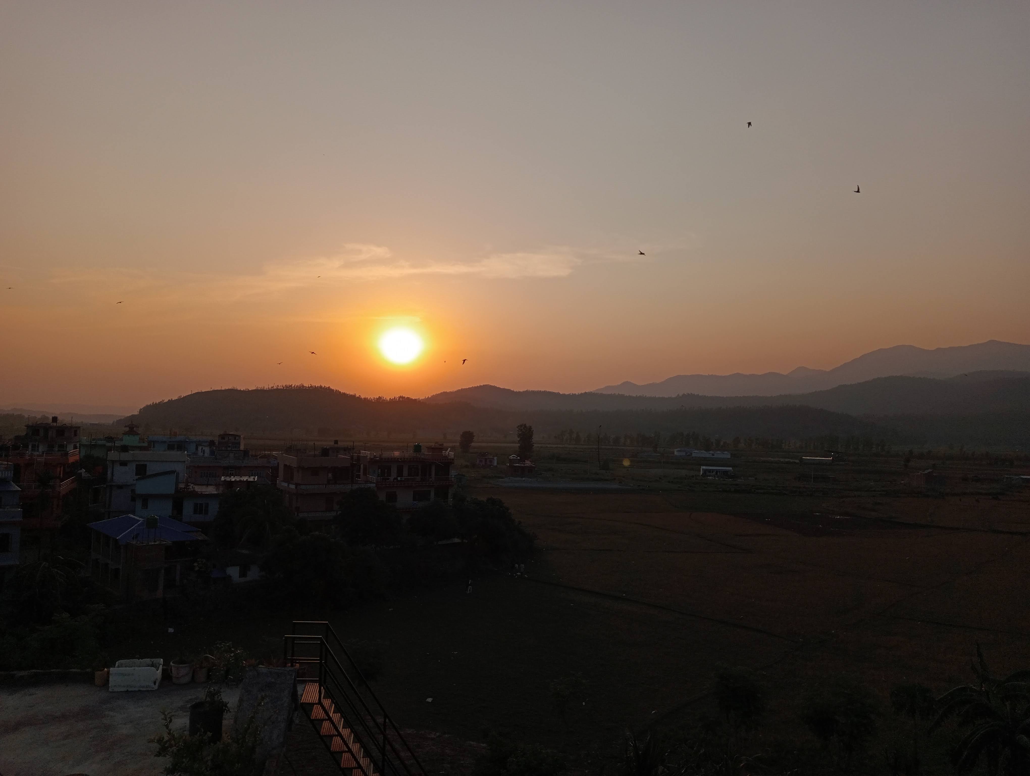 Sunset over distant mountains and village rooftops