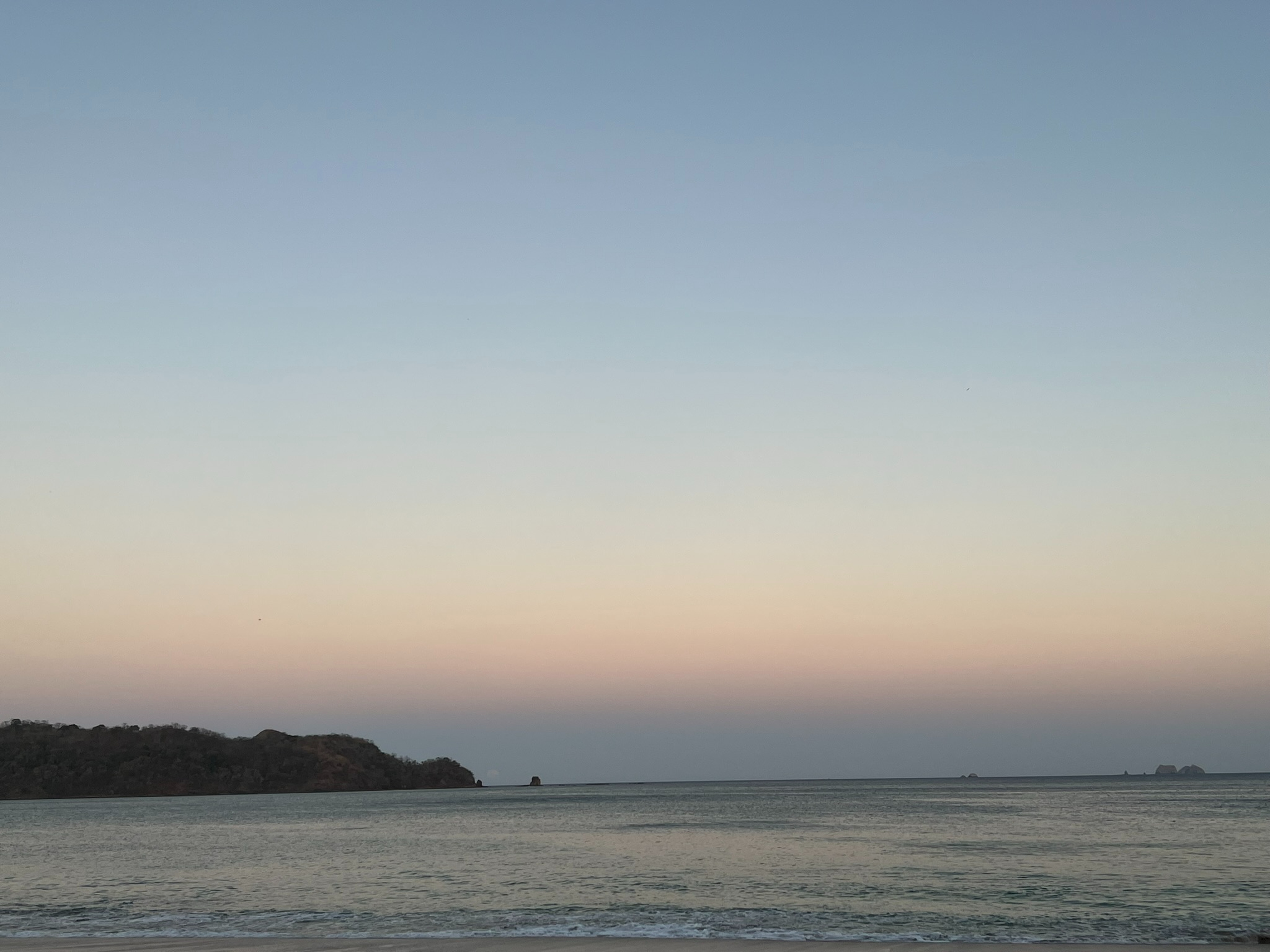 Peaceful beach with calm waves and a pastel sunset sky.