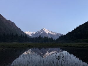 Snow capped mountain peaks at dawn, reflected in a still water body. 