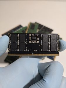 A close-up image of a hand in blue glove holding a SODIMM RAM module of DDR5 architecture.