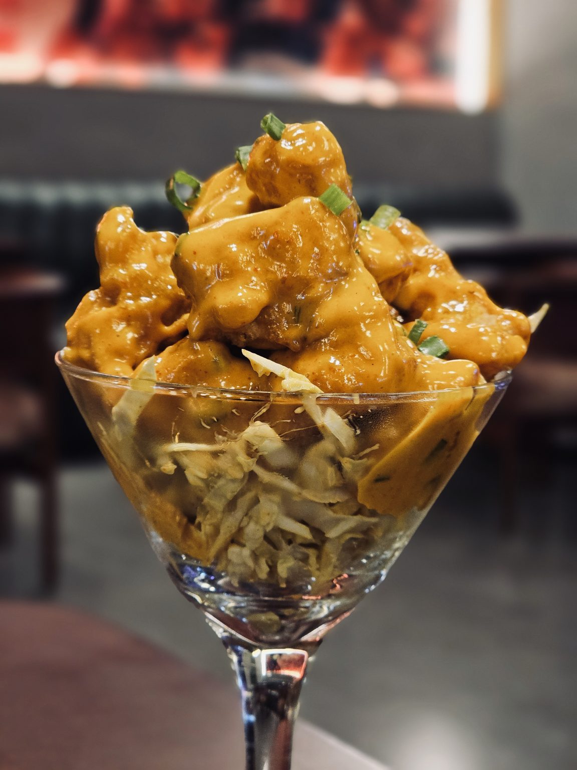 Golden, crispy chicken dynamite pieces, covered in a creamy sauce, are served in a clear glass bowl over shredded cabbage. The presentation is elegant and highlights the rich texture of the dish. Captured in Mankavu, Kozhikode.