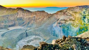 
A wide view of a volcanic crater at sunset, showcasing jagged peaks surrounding a deep, circular basin.