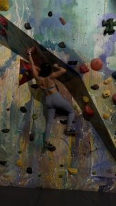Person climbing a colorful indoor rock climbing wall.
