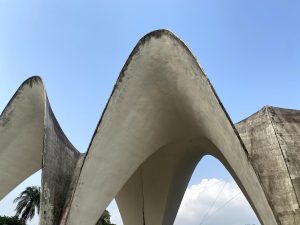 Low-angle view of Kamalapur Railway Station’s concrete parabolic arches against a clear blue sky.
