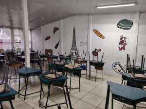 
Empty classroom with stacked desks and colorful wall murals.