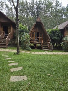 Three bamboo huts on stilts in a grassy area with a stone path.