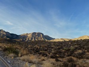 Sunlit desert mountains rising above rocky terrain under a clear blue sky.
