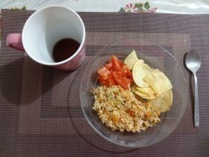 
Plate of rice with tuna, vegetables, tomato slices, and potato chips, served with a cup of tea.