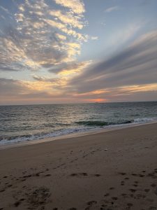 A picture of the edge of the sea with a cloudy sky, a mild sunset view with a ship at a far distance.