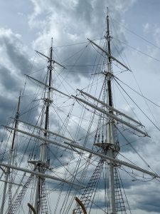 The masts and sail rigging on a tall ship with huge dark billowy clouds in the sky.