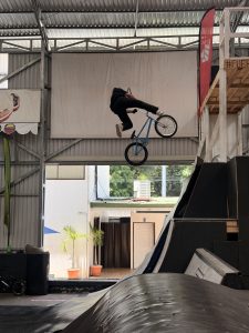 BMX rider performing an aerial trick inside a skate park with a blue bike and indoor structures.