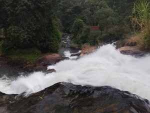 A cascading waterfall pours over smooth black rocks, generating white foamy water as it tumbles down.