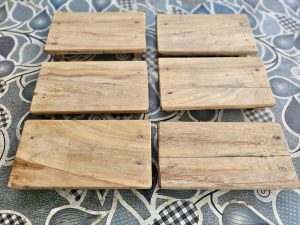 Six handcrafted wooden display stands (wood risers) are neatly arranged, highlighting the natural wood grain and simple design. The image showcases traditional craftsmanship with clean composition. Captured in Pantheeramkavu, Kozhikode, Kerala.