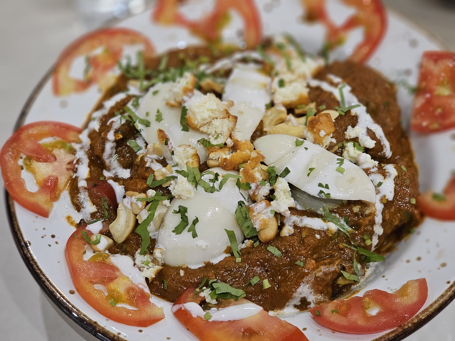 A rich and creamy chicken curry (chicken maharaja) topped with boiled eggs, fresh coriander, cashews, and a drizzle of cream. Fresh tomato slices add color to this delicious dish. Captured in Nadakkavu, Kozhikode, Kerala.