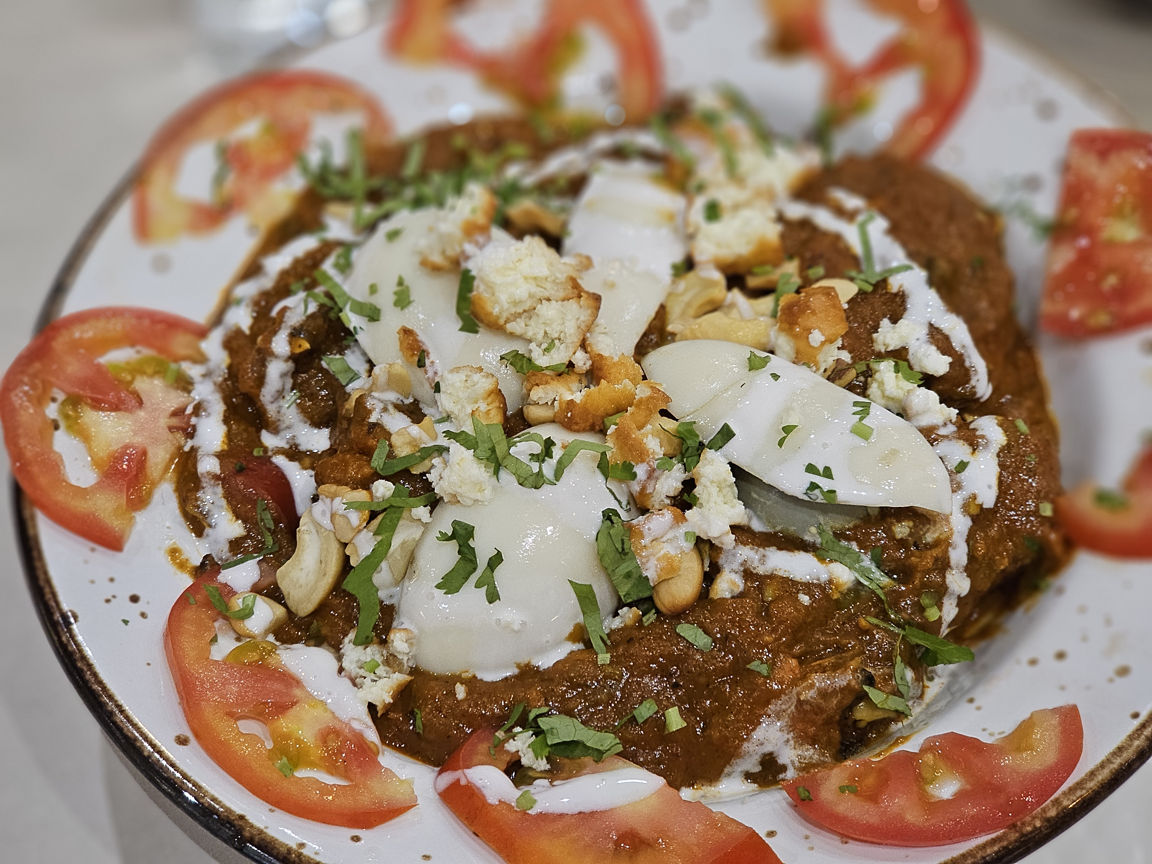 A rich and creamy chicken curry (chicken maharaja) topped with boiled eggs, fresh coriander, cashews, and a drizzle of cream. Fresh tomato slices add color to this delicious dish. Captured in Nadakkavu, Kozhikode, Kerala.