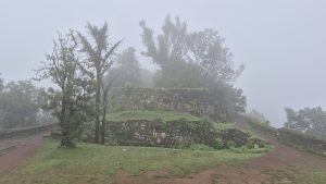 A misty landscape featuring ancient stone ruins set against a backdrop of dense fog.
