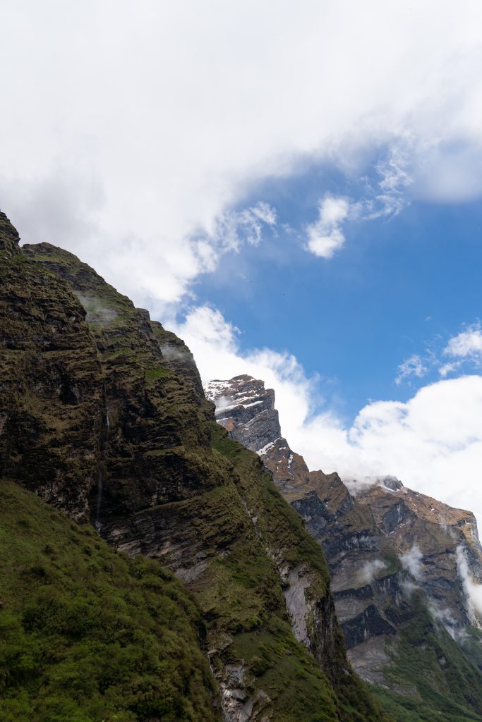 Steep mountain cliffs with patches of green vegetation rise under a bright blue sky with scattered clouds
