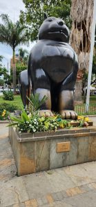 A large bronze statue of a cat sits prominently in a public area. The cat has a rounded, stylized appearance with a smooth, shiny surface. 