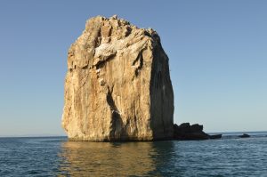Large rock sea rising from calm ocean waters under a clear blue sky.
