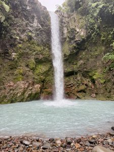 Waterfall flowing into a turquoise pool surrounded by moss-covered volcanic rocks and lush forest in Costa Rica.
