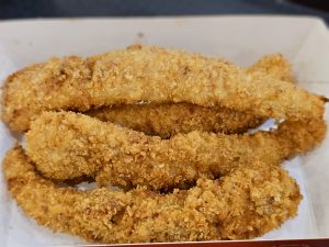 Golden-brown, crispy fried fish (Basa) strips are served fresh, with a crunchy coating and a perfectly cooked look. The simple presentation highlights their delicious texture. Captured in Palazhi, Kozhikode.
