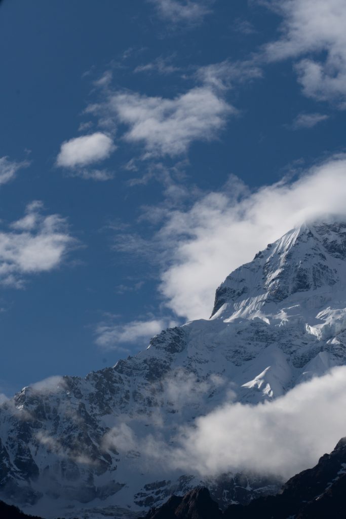 Snow-capped mountain ridge with rocky exposed peaks under a blue sky with scattered clouds