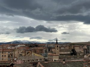 View of Segovia, Spain, with historic buildings, church tower, and snow-covered mountains in the background.