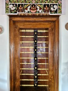 A beautifully crafted wooden doorway is topped with colorful carvings of birds, elephants, and traditional figures. The detailed artwork reflects Kerala's rich architectural heritage. Captured at Mangode, Puthunagaram, Palakkad.