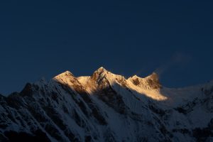 Snow-covered mountain peaks lit gold by low sunlight against a dark blue sky