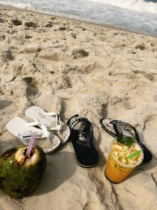 A sandy beach scene featuring two pairs of flip-flops—one white and one dark blue—scattered on the soft sand.