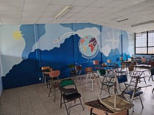 
Classroom with stacked desks and a colorful mural of the sun, globe, and airplane.