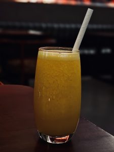 A chilled glass of fresh orange juice is served with a paper straw, showing its refreshing color and smooth texture. The simple composition creates a clean and appealing drink photograph. Captured in Mankavu, Kozhikode.