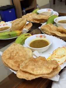 Traditional breakfast plates with puffed fried bread, lentil curry, fried egg, and green bananas served on a dining table.