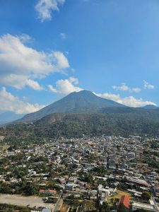 A town spread out at the base of a towering green volcano under a vivid blue sky with scattered clouds