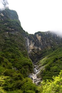 Waterfall cascading down a rocky cliff between forested mountain slopes
