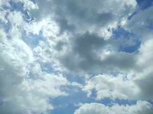 wide-angle low-angle shot of a vibrant blue sky filled with a mix of bright white and heavy grey storm clouds, showing sunlight filtering through the edges.
