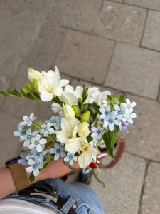Small bouquet of white freesias and pale blue flowers held in hand on a city sidewalk