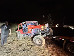 Red off-road Jeep climbing onto a trailer at night.
