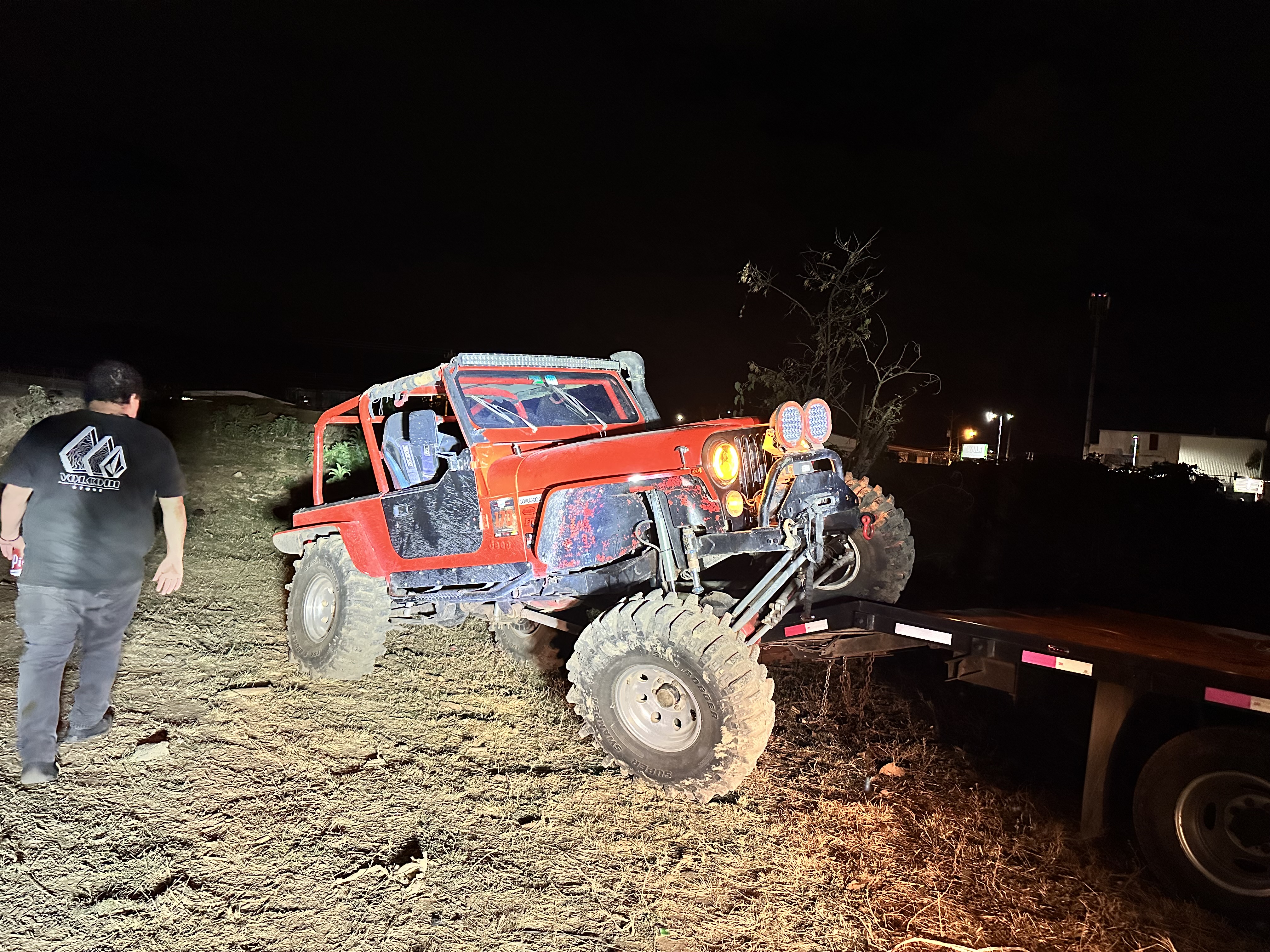 Red off-road Jeep climbing onto a trailer at night.
