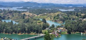 A panoramic view of a lush landscape, featuring a series of winding lakes surrounded by rolling hills and mountains in the background.