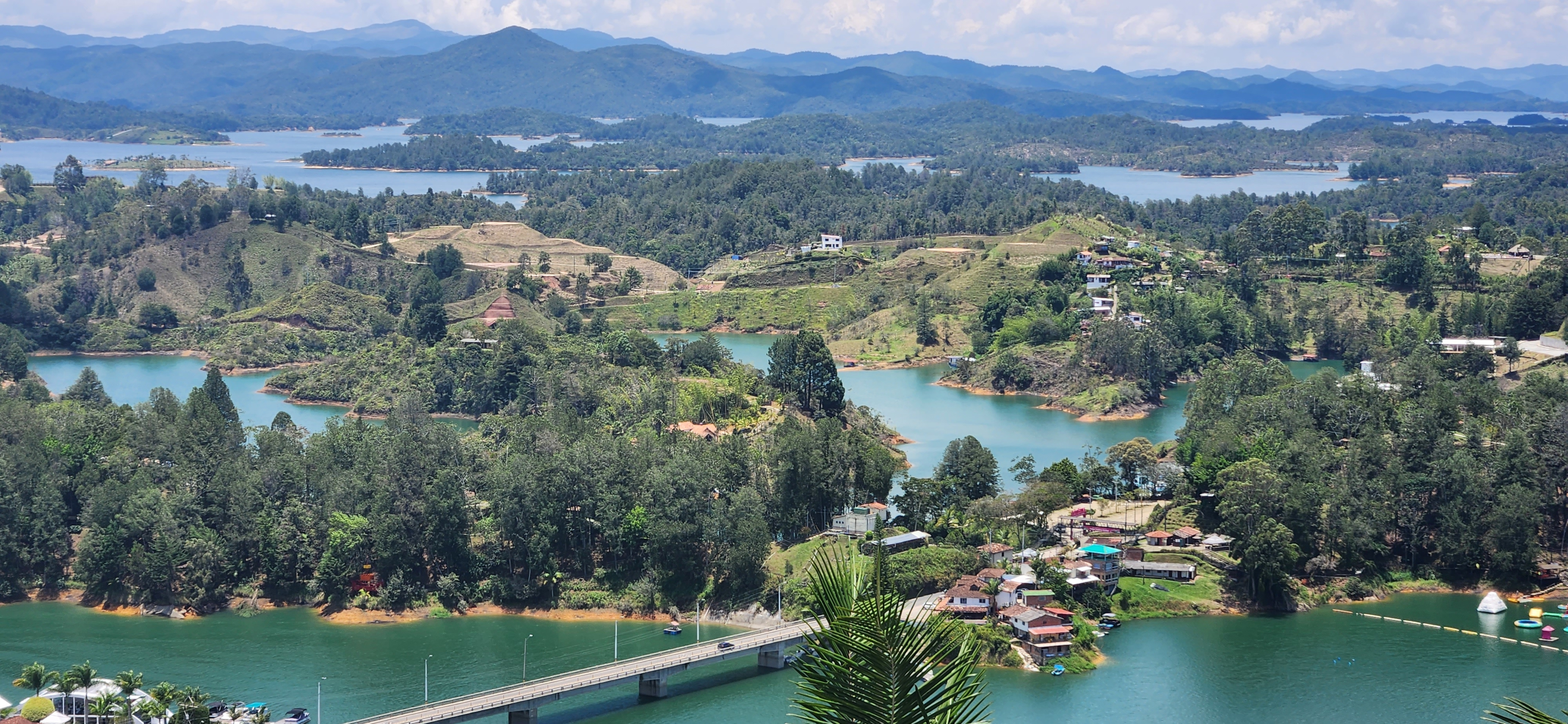 A panoramic view of a lush landscape, featuring a series of winding lakes surrounded by rolling hills and mountains in the background.