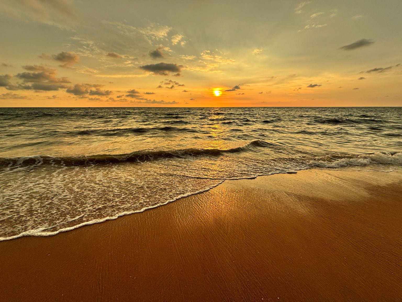 Golden sunset over Negombo Beach with gentle waves curling onto warm sand.