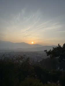 Sunset over a cityscape with distant mountains and wispy clouds. 