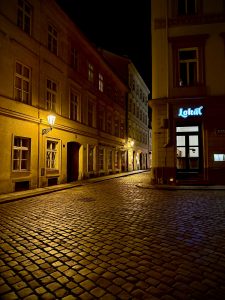 Cobbled street illuminated by historic street lamps between old buildings at night in Prague, Czech Republic.