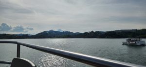Peaceful lake with a boat sailing, distant green hills, and a cloudy sky.