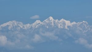 Mountains in Nepal - Snow-capped mountain peaks rise above a blanket of white clouds beneath a clear blue sky, with bright snow contrasting against rugged rocky slopes.