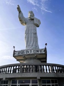 Large white Jesus Christ statue on a pedestal overlooking the landscape under a blue sky.