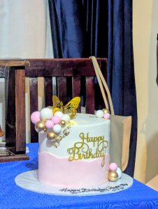 A white and pink birthday cake with "Happy Birthday" in gold script. 